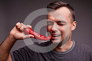 Funny guy eating red chili pepper on a gray background. Handsome man with spicy, hot pepper. Spiciness concept.