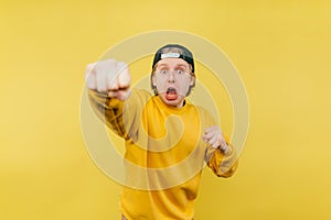 Funny guy with a scared face shows a fist to the camera on a yellow background