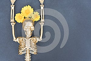 Funny halloween composition with golden skeleton wearing wreath of flowers over gray concrete background with copy space