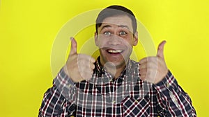 Funny handsome guy smiles and shows thumb up with both hands. Portrait on yellow background.