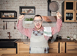 Funny handsome screaming angry man wearing pinafore with kitchen utensils