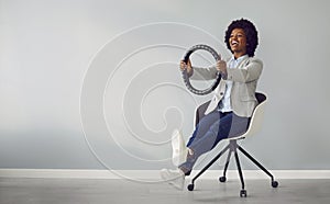 Funny, happy African American woman sitting on a chair and pretending to drive an invisible car