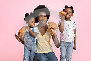 Funny happy african family, mother and two little kids girls, wearing colorful outfits, posing to camera on pink