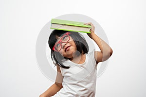Funny and Happy Asian little preschool girl wearing red glasses holding a green book on the head, on white isolated background.