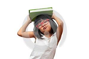 Funny and Happy Asian little preschool girl wearing red glasses holding a green book on the head, on white isolated background.