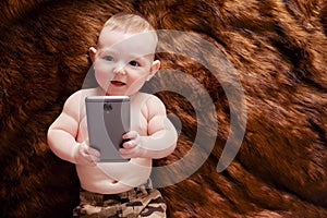 Funny happy baby boy with a phone in his hands on a fur carpet. Smiling child holds a smartphone, top view