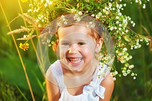 funny happy baby child girl in a wreath on nature laughing in summer