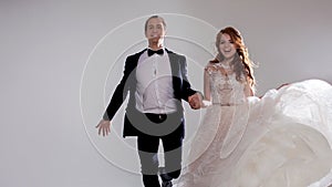 Funny and happy bride and groom, dance and jump with happiness, married. Studio portrait, light background