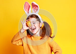 Funny happy child girl with easter eggs and bunny ears on yellow