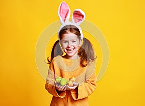 Funny happy child girl with easter eggs and bunny ears on yellow