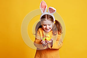 Funny happy child girl with easter eggs and bunny ears on yellow