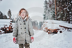 Funny happy child girl portrait on the walk in winter snowy forest with tree felling on background