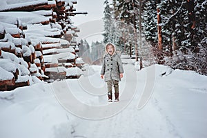 Funny happy child girl portrait on the walk in winter snowy forest with tree felling on background