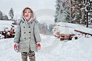 Funny happy child girl portrait on the walk in winter snowy forest with tree felling on background