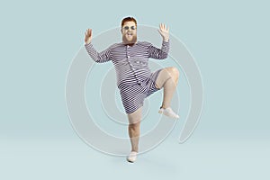 Funny happy chubby young guy in striped swimsuit and sunglasses dancing in studio