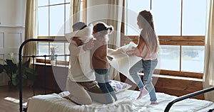 Funny happy dad playing pillow fight with daughters in bed