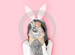 funny happy girl with bunny ears holding grey rabbit on pink background.