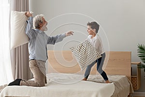 Funny happy grandfather and grandson enjoy pillow fight on bed