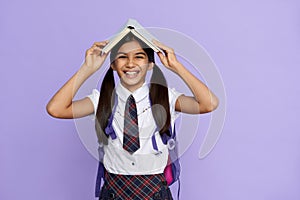 Funny happy indian child primary school girl laughing holding book over head.