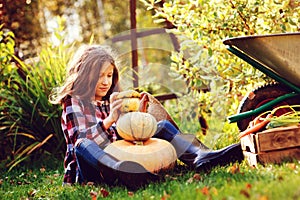 Funny happy kid girl playing with pumpkins and building `snowman` in autumn garden