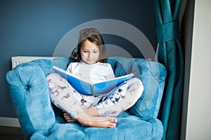 Funny happy little girl reading a book and playing in bed. Kids play at home. White nursery. Child in sunny bedroom. Children read