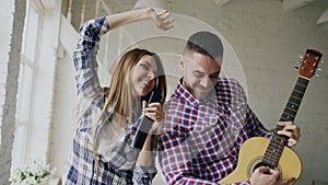 Funny happy and loving couple dancing and playing guitar. Man and woman have fun during their holiday at home