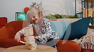 Funny happy one teenage kid girl play wooden tower blocks bricks game at home in modern living room