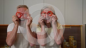 Funny happy retired grandma grandpa Caucasian old man woman having fun together make red paprika glasses peppers circles