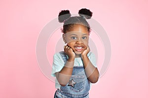 Funny happy smiling little cute African-american girl, with afro hair in two ponytails, posing with her arms under face