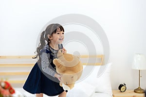 Funny happy toddler girl jumping and playing with her toy teddy bear in bed. Kids play at home.