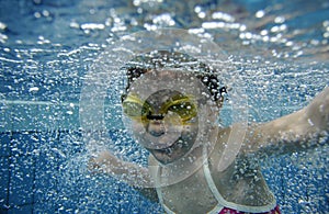 Funny happy toddler girl swimming underwater in a