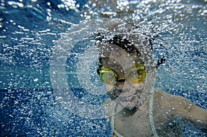 Funny happy toddler girl swimming underwater in a pool with lots of air bubbles