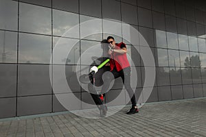 Funny happy young man in a stylish red denim vest in black vintage jeans in gym shoes in sunglasses posing