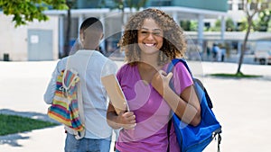 Funny hispanic female student with backpack and paperwork infront of university