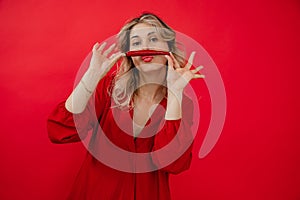 Funny, humorous, confident blonde woman in red dress hold red chili pepper in hands under nose like mustache. Hot news