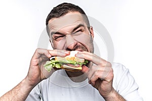 Funny and hungry guy is eating some fast food. He is hungry like a wolf. Man is biting sandwich very hard. Isolated on