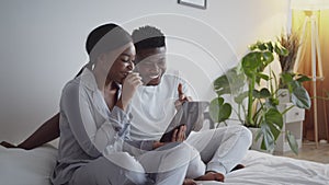 Funny internet content. Young happy african american man and woman watching social media on digital tablet in bed