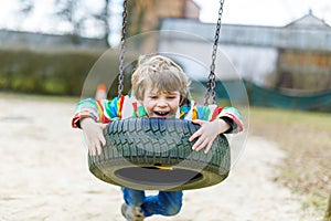 Funny kid boy having fun with chain swing on outdoor playground