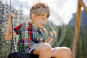 Funny kid boy having fun with chain swing on outdoor playground while being wet splashed with water. child swinging on