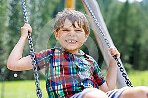Funny kid boy having fun with chain swing on outdoor playground while being wet splashed with water. child swinging on