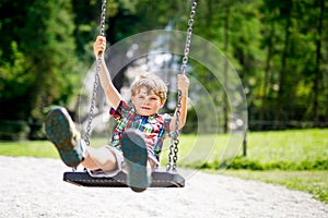 Funny kid boy having fun with chain swing on outdoor playground while being wet splashed with water