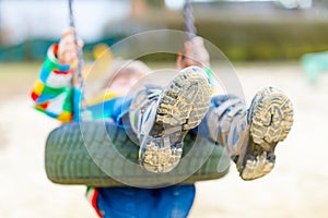 Funny kid boy having fun with chain swing on outdoor playground. child swinging on warm sunny spring or autumn day