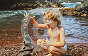 Funny kid boy making stack of pebbles stone against sea background for spa, balance, meditation and zen theme. Child