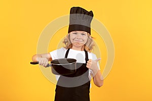 Funny kid chef cook with kitchen pot stockpot. Kid in cooker uniform and chef hat preparing food on studio color photo