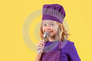 Funny kid chef cook with spoon, studio portrait. Excited chef cook. Child wearing cooker uniform and chef hat preparing