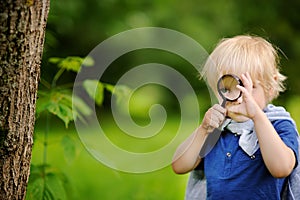 Funny kid exploring nature with magnifying glass.