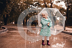 Funny kid girl 4-5 year old wear rainboots and raincoat walk in puddler outdoors close up. Autumn season concept