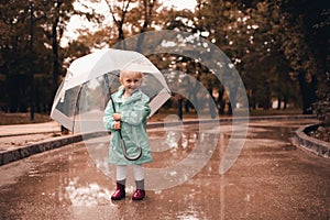 Funny kid girl 4-5 year old wear rainboots and raincoat walk in puddler outdoors close up. Autumn season concept