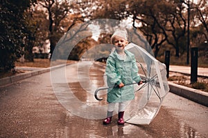 Funny kid girl 4-5 year old wear rainboots and raincoat walk in puddler outdoors close up. Autumn season concept
