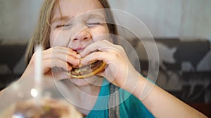 Funny kid girl eats a delicious burger in a cafe. fast food cafes.